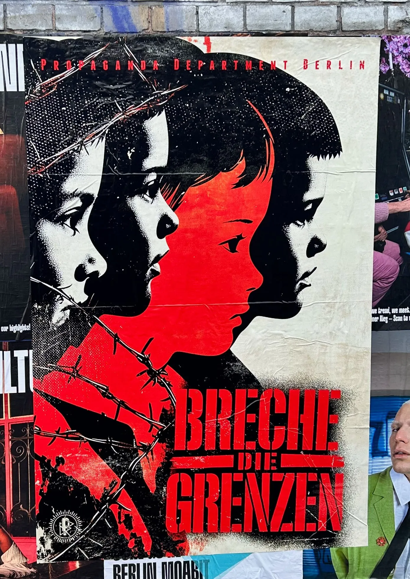 The poster: children behind barbed wire under the red words Breche die Grenzen